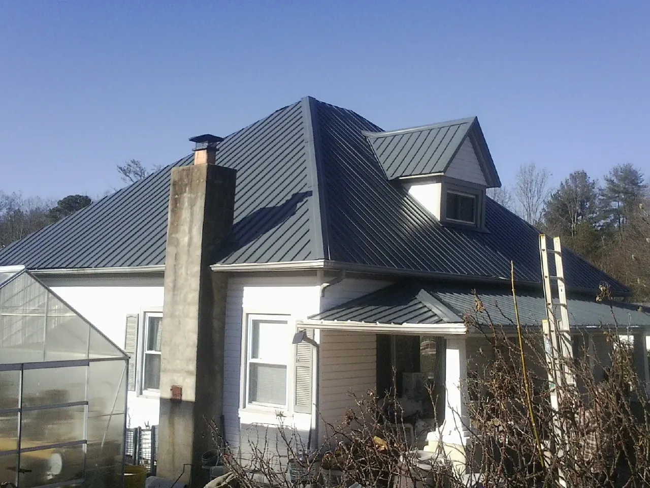 Dark blue standing seam metal roof on a white farmhouse with dormer — Slate & Tile Roof Repair by Roofing Brothers in Greycliff