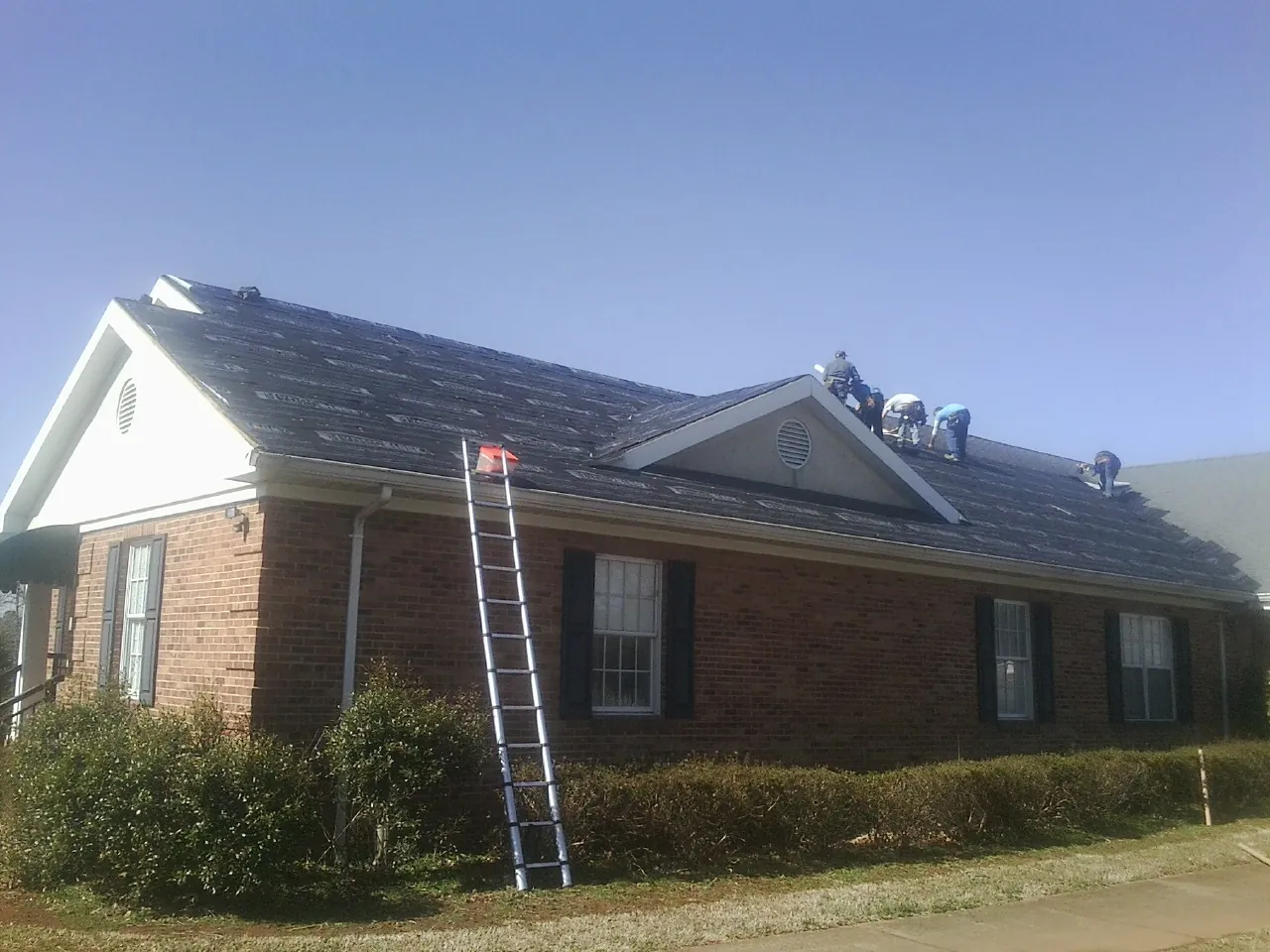 Crew tearing shingles off a brick ranch roof with a ladder set — Emergency Roof Repair work by our crew in Greycliff