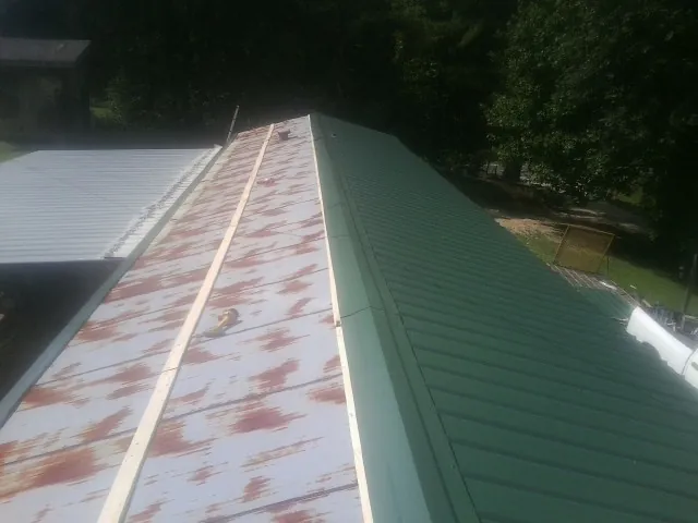 Old rusted panels beside newly installed green metal roofing — Wind Damage Roof Repair by Roofing Brothers in Greycliff