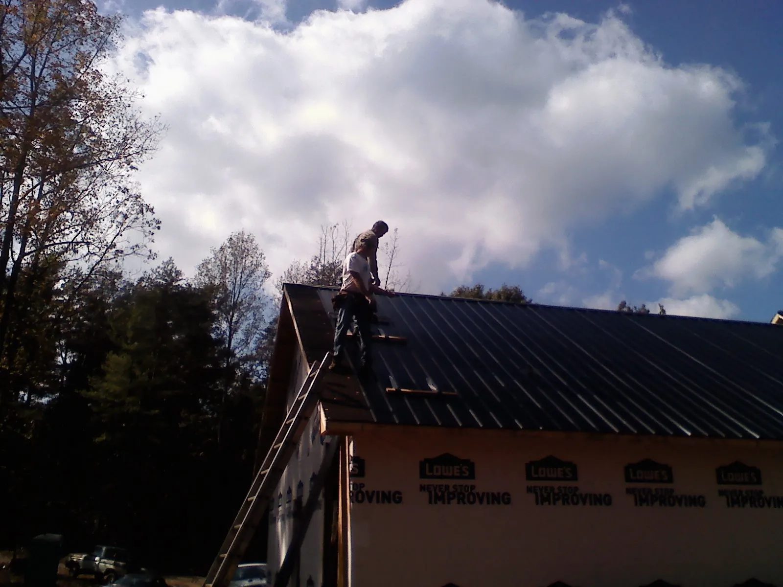 Roofer fastening dark metal panels high against a cloudy sky, from a Roof Inspection job in Greycliff