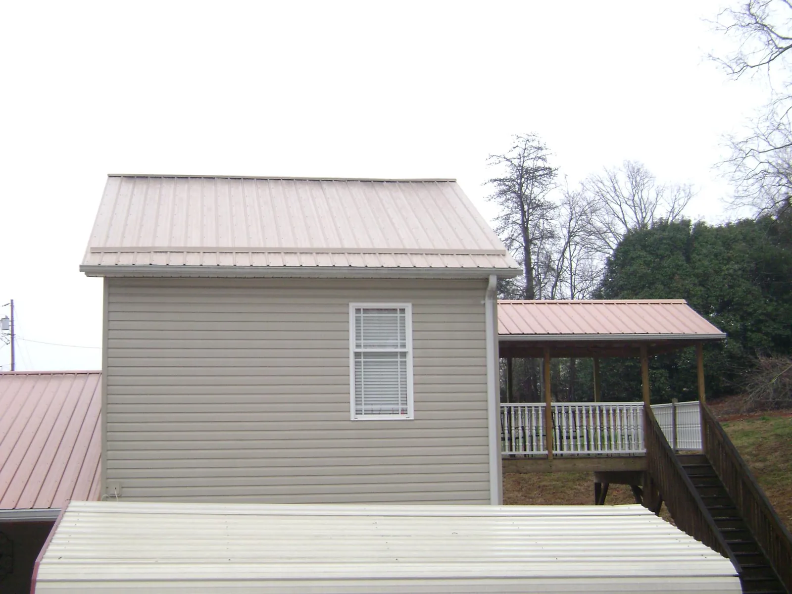 Tan metal roofs on a two story addition and attached porch, from a Roof Replacement job in Greycliff